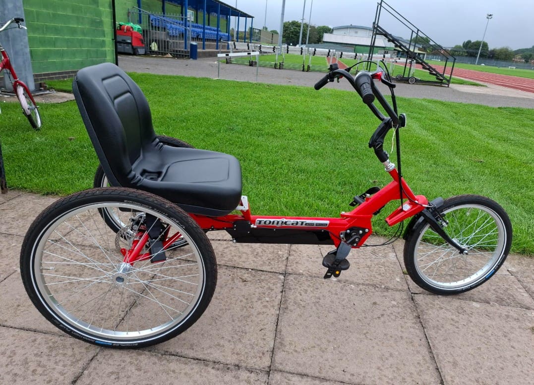 Red Tomcat adapted tricycle with a supportive seat beside the track at Shobnall Leisure Complex